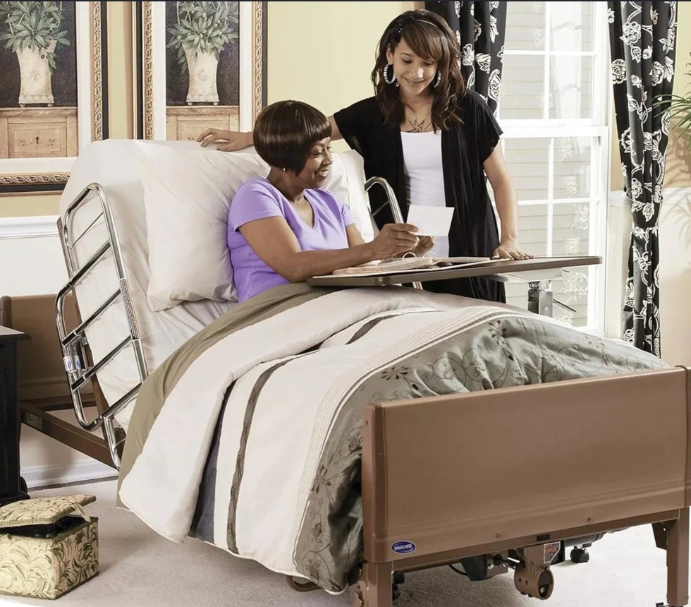 Woman sitting up in a home medical bed with a visitor beside her